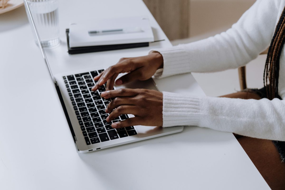 A person's hands typing on a laptop keyboard at a desk